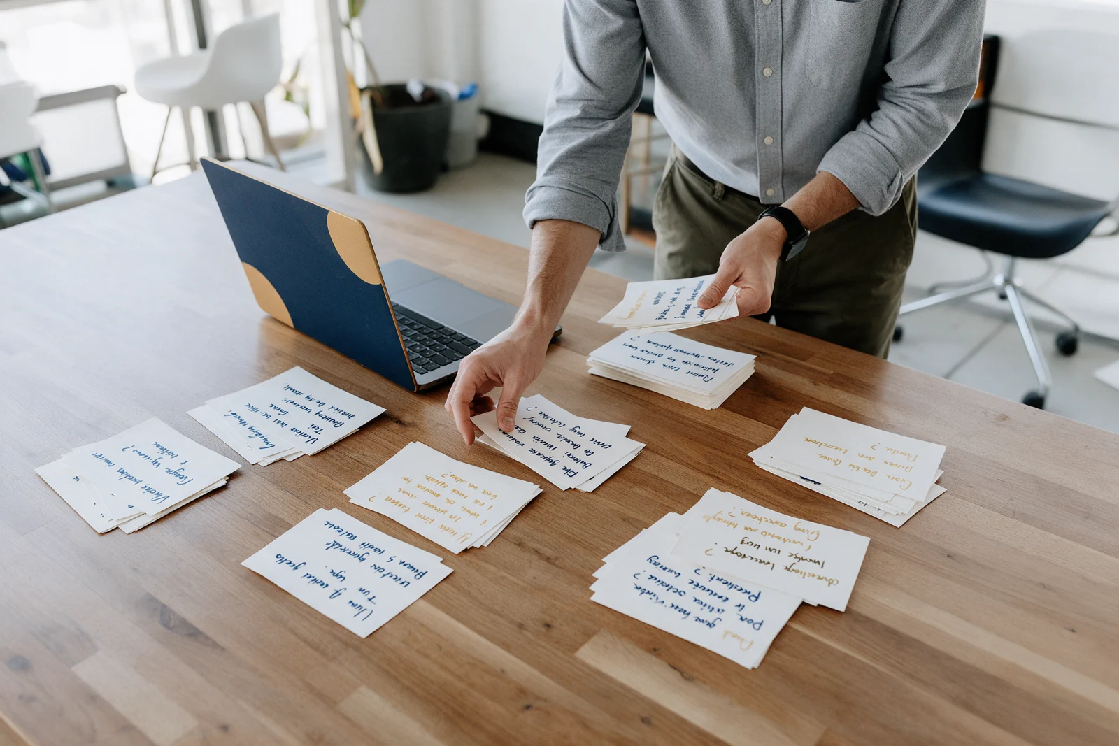Consultant sorting handwritten customer question cards into groups on a large desk beside an open laptop in a bright office