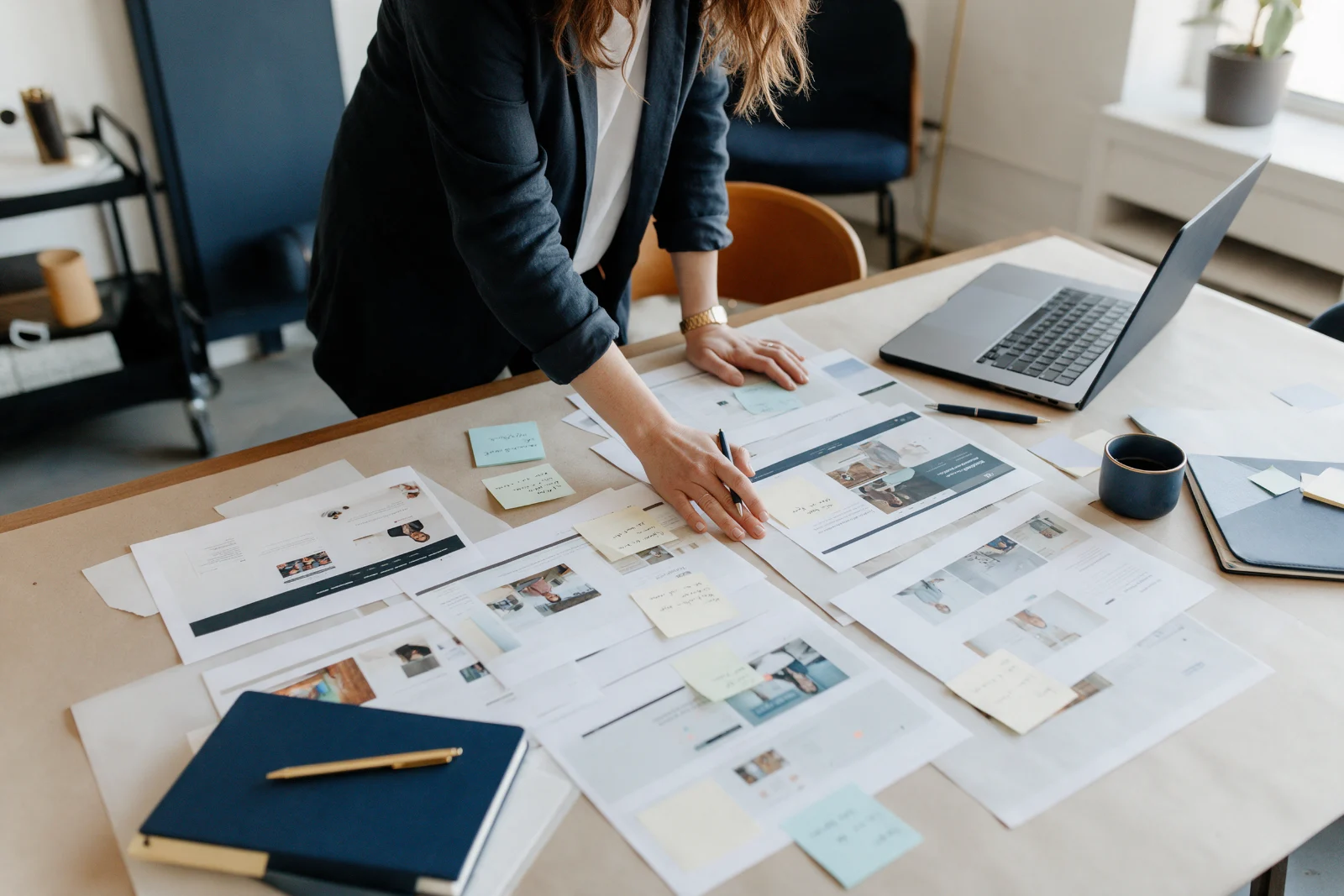 Marketing consultant comparing several printed web pages laid out on a table to see which sources agree, with a laptop open nearby