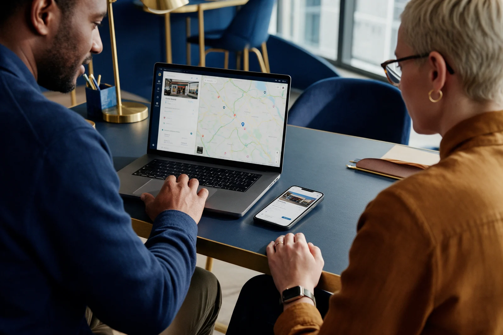 Two colleagues comparing a business listing on a laptop map view and a smartphone side by side at a desk in a modern office