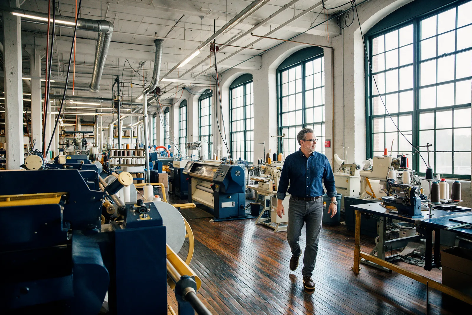 Manufacturing business owner walking through a converted textile mill with modern machinery and tall arched windows