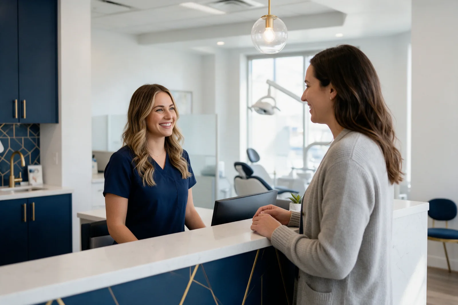 Smiling receptionist at a modern dental practice front desk greeting a patient in a bright interior with navy details