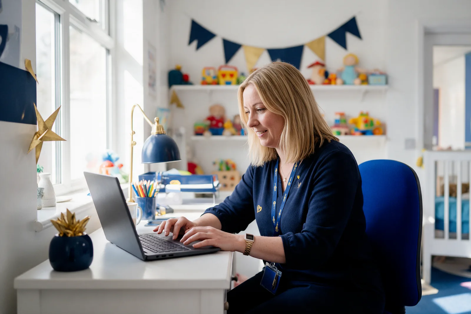 Children's nursery manager working on a laptop in a bright, colourful nursery office with toys on the shelves behind