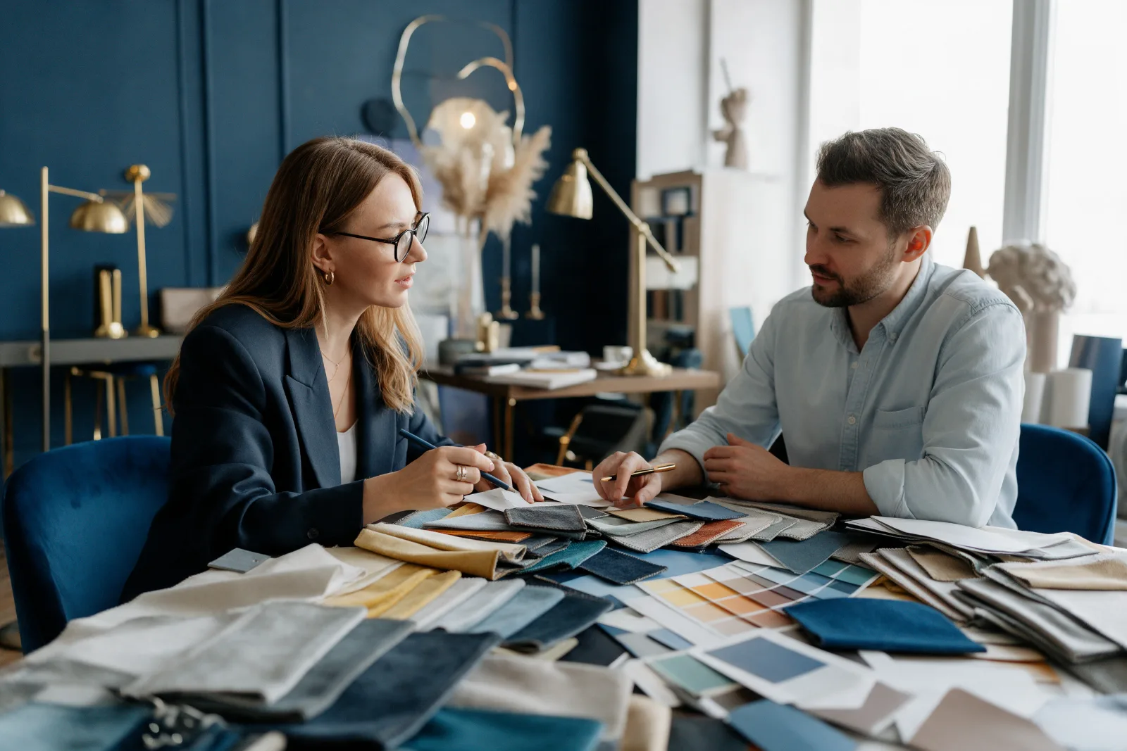 Interior designer meeting a client at a table covered with fabric swatches and colour samples in an elegant studio