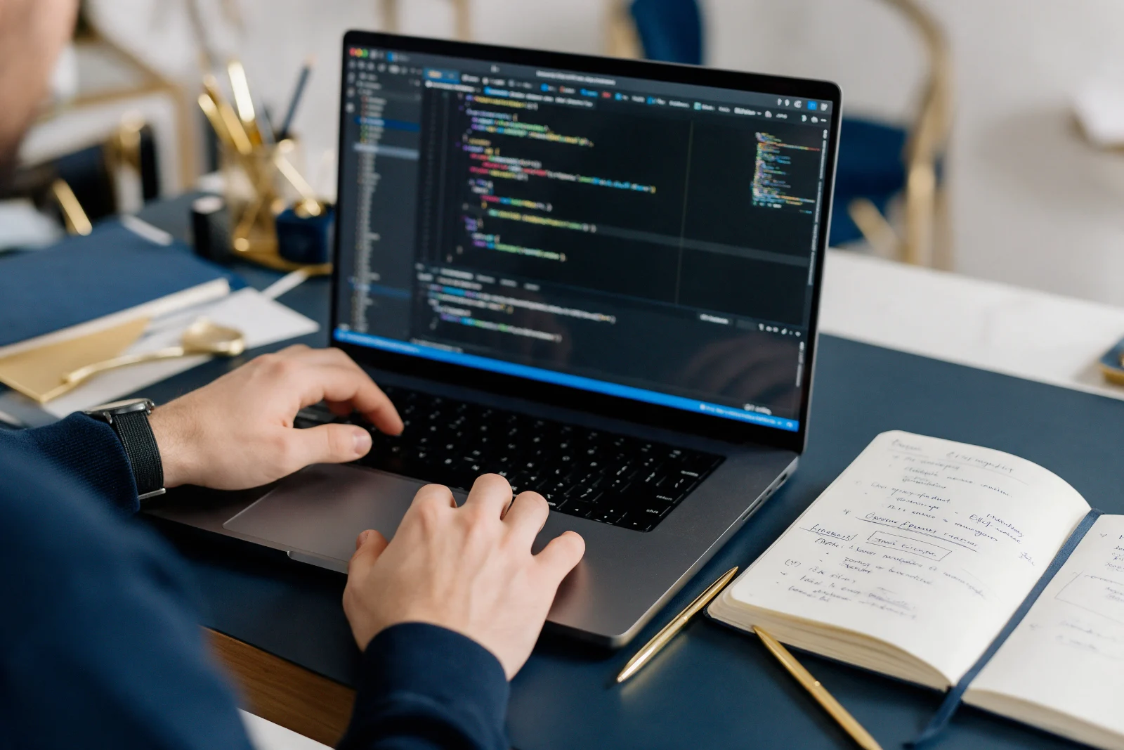 Developer inspecting page code in browser developer tools on a laptop, with a notebook of audit notes and a pen beside the keyboard