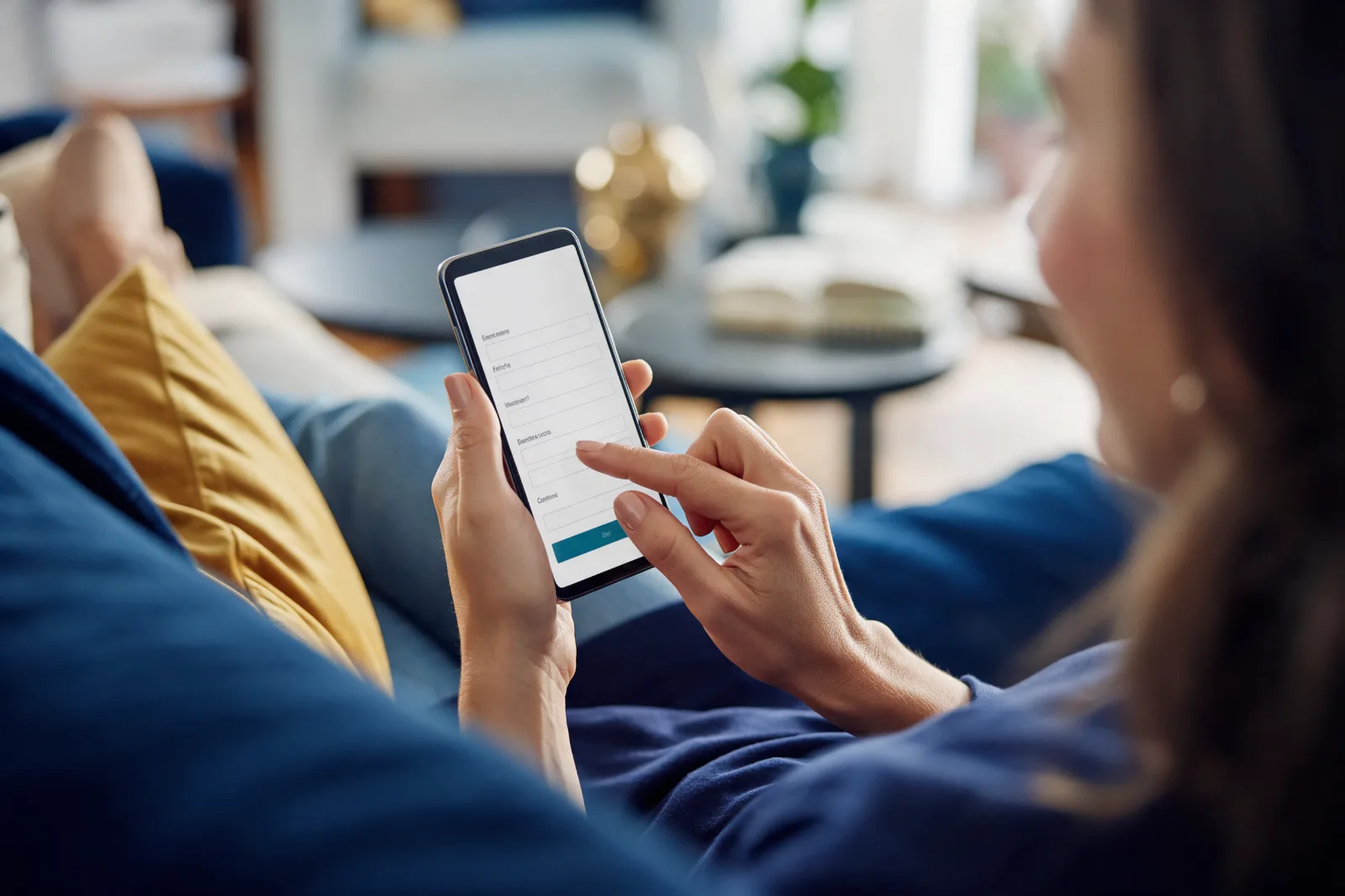Woman relaxing on a sofa at home and filling in a short enquiry form on her smartphone, with a close focus on her hands
