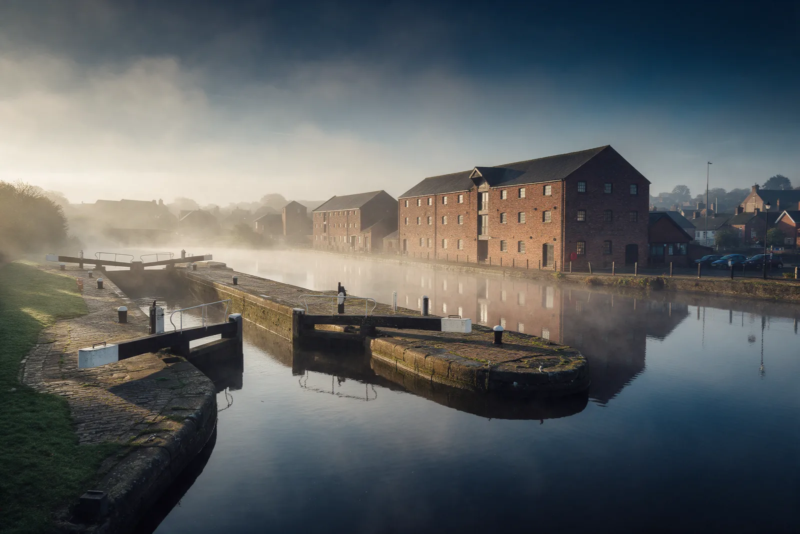 Restored canal with old stone locks and red brick warehouse buildings beside calm water in light morning mist
