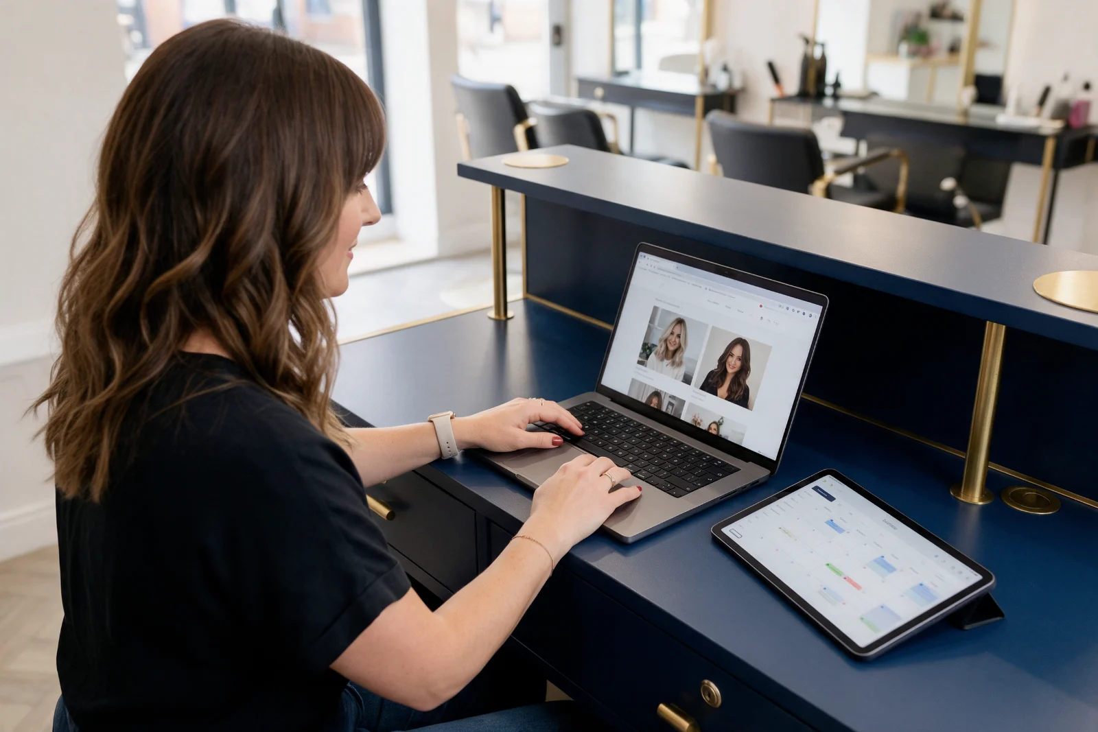 Salon owner at her reception desk updating prices on her Wix website from a laptop, with a booking calendar open beside her